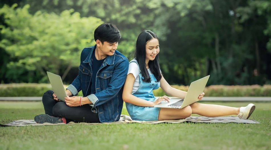 Ausländische Studenten Asiatisches Paar sitzt im Park und nutzt einen Laptop, um gemeinsam zu arbeiten oder Informationen zu suchen.