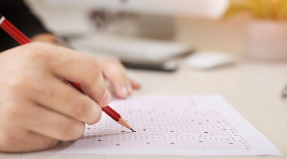 Multiple-Choice-Test Eine Person schreibt mit einem Bleistift auf ein Stück Papier.