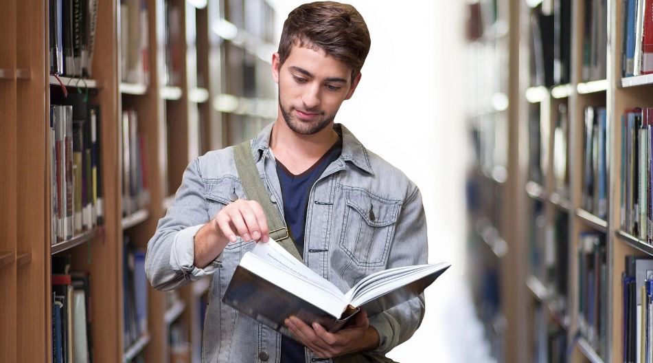 Studium Ein Mann liest ein Buch in einer Bibliothek, umgeben von Regalen voller Bücher und einer ruhigen Atmosphäre.