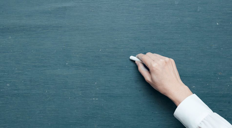 Schreibende Hand an Tafel Eine Person notiert etwas mit weißer Kreide auf einer Tafel.