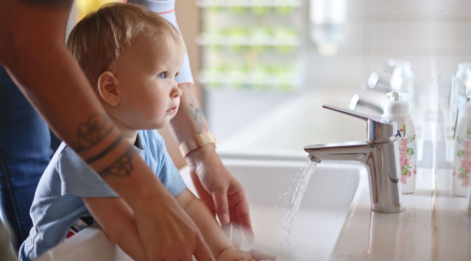 Eine Erzieherin hilft einem kleinen Kind am Kinderwaschbecken beim Waschen der Hände. Eine Erzieherin hilft einem kleinen Kind am Kinderwaschbecken beim Waschen der Hände.