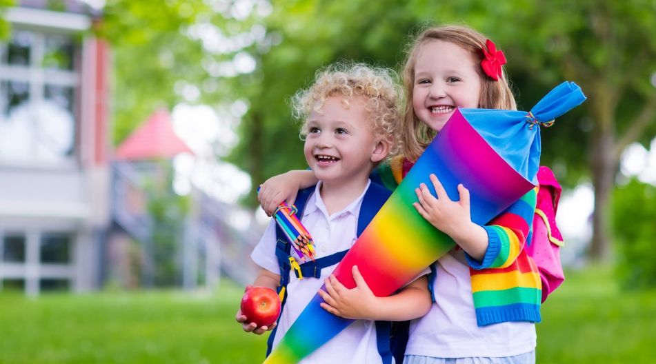 Zwei lachende Kinder mit Schultüte und Rucksäcken vor einer Schule. Zwei lachende Kinder mit Schultüte und Rucksäcken vor einer Schule.