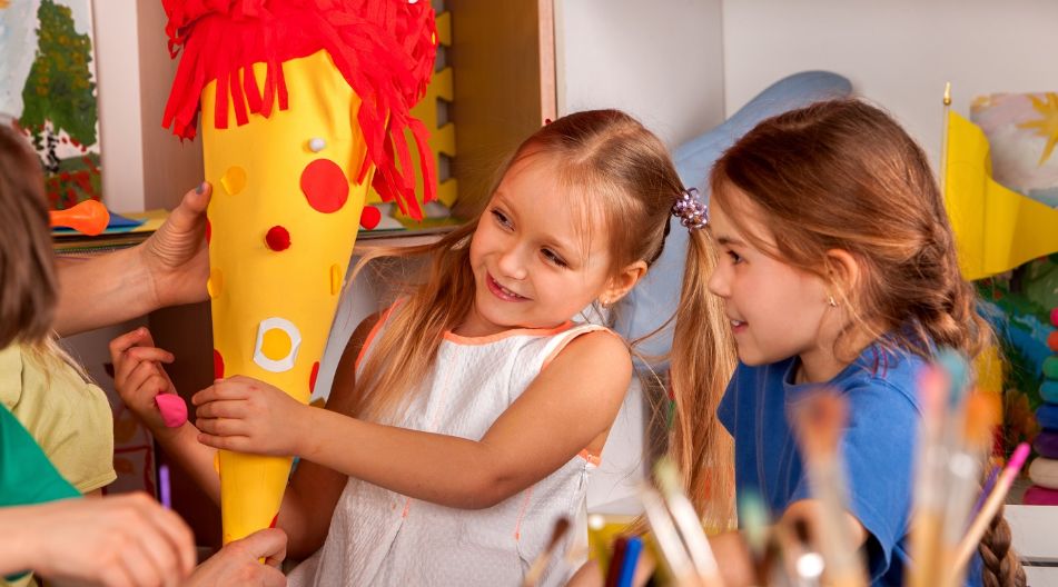 Zwei Mädchen freuen sich über eine bunte Schultüte, die sie zusammen mit einer Lehrkraft halten. Zwei Mädchen freuen sich über eine bunte Schultüte, die sie zusammen mit einer Lehrkraft halten.