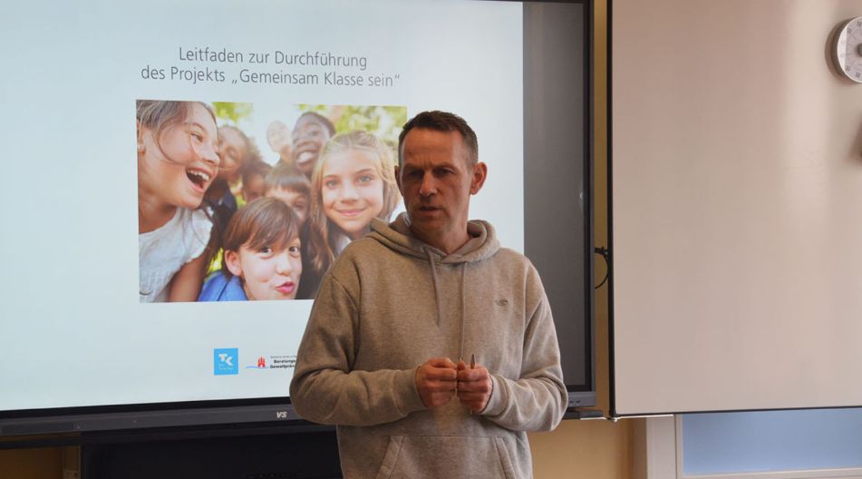 Präsentation des Projektes Gemeinsam Klasse sein der 6c der Werner-von-Siemens-Schule Ein Mann steht vor einem Bildschirm und präsentiert Informationen während einer Präsentation.