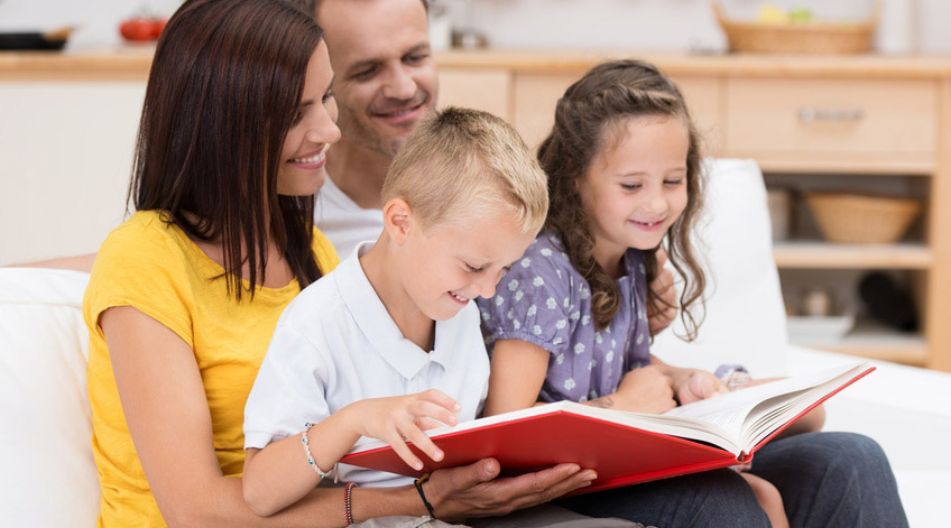 ine Familie sitzt auf dem Sofa und liest gemeinsam in einem großen roten Buch. Die Eltern lächeln, während die beiden Kinder, ein Junge und ein Mädchen, begeistert auf die Seiten schauen. ine Familie sitzt auf dem Sofa und liest gemeinsam in einem großen roten Buch. Die Eltern lächeln, während die beiden Kinder, ein Junge und ein Mädchen, begeistert auf die Seiten schauen.