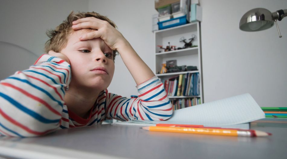 Ein Junge sitzt an einem Schreibtisch, stützt seinen Kopf in die Hände und wirkt nachdenklich oder besorgt. Ein Junge sitzt an einem Schreibtisch, stützt seinen Kopf in die Hände und wirkt nachdenklich oder besorgt.