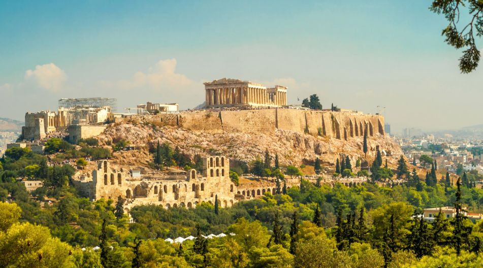 Blick auf die Akropolis von Athen, ein berühmtes antikes Bauwerk mit dem Parthenon an der Spitze eines felsigen Hügels, umgeben von üppigem Grün und der Stadt im Hintergrund. Blick auf die Akropolis von Athen, ein berühmtes antikes Bauwerk mit dem Parthenon an der Spitze eines felsigen Hügels, umgeben von üppigem Grün und der Stadt im Hintergrund.